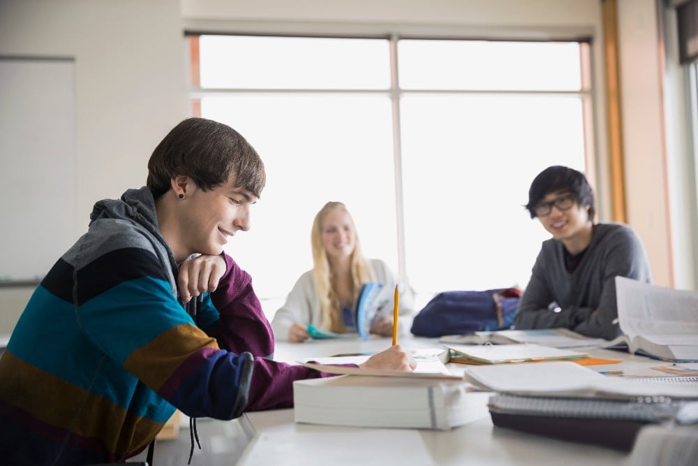 Drie leerlingen zitten lachend aan een tafel tijdens de ideale les.