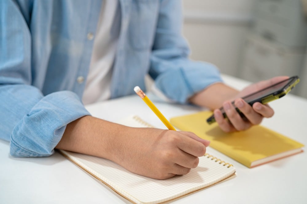 Student met in een hand telefoon en andere hand een potlood