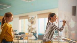 Meisje tekent op een bord en een ander meisje kijkt toe