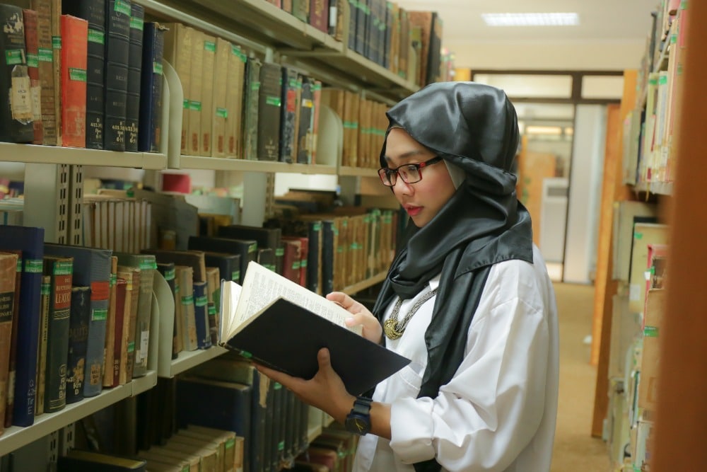 Jonge mevrouw slaat boek open in de bibliotheek