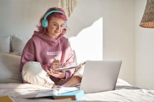 Een mbo student zit op haar bed met een laptop te studeren