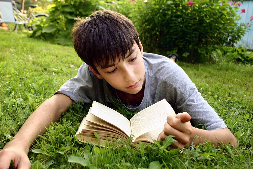 jongen leest boek in het gras