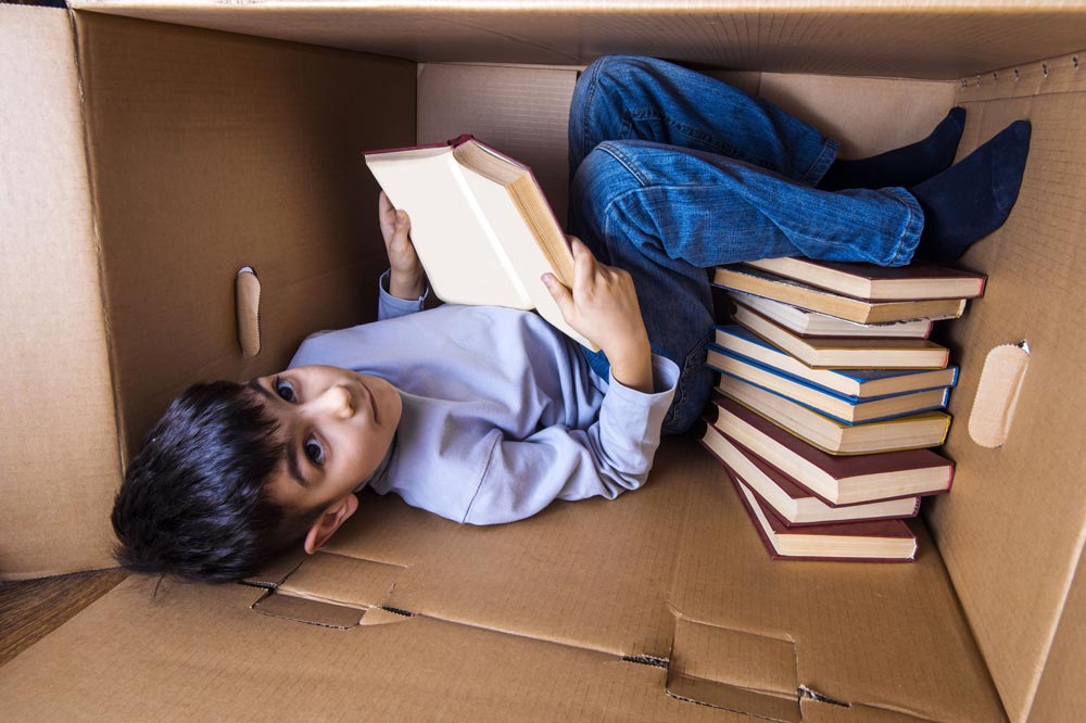 Een jongen die leest in een kartonnen doos