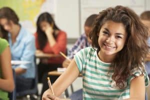 Een scholiere zit in de klas en kijk glimlachend in de camera