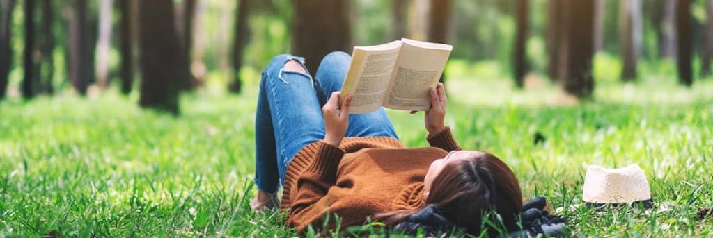 Een tiener ligt in de natuur te lezen