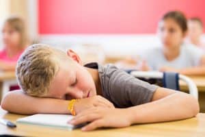Een kind ligt te slapen op zijn tafeltje in de klas