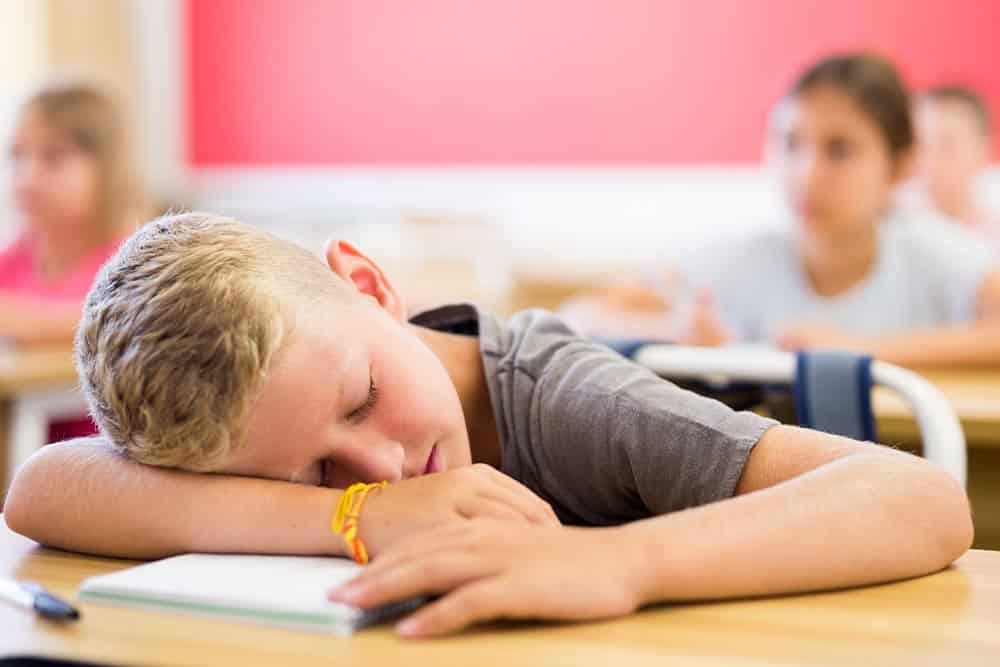 Een kind ligt te slapen op zijn tafeltje in de klas