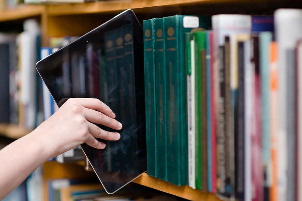 Een tablet wordt in de schoolbibliotheek tussen de boeken gezet