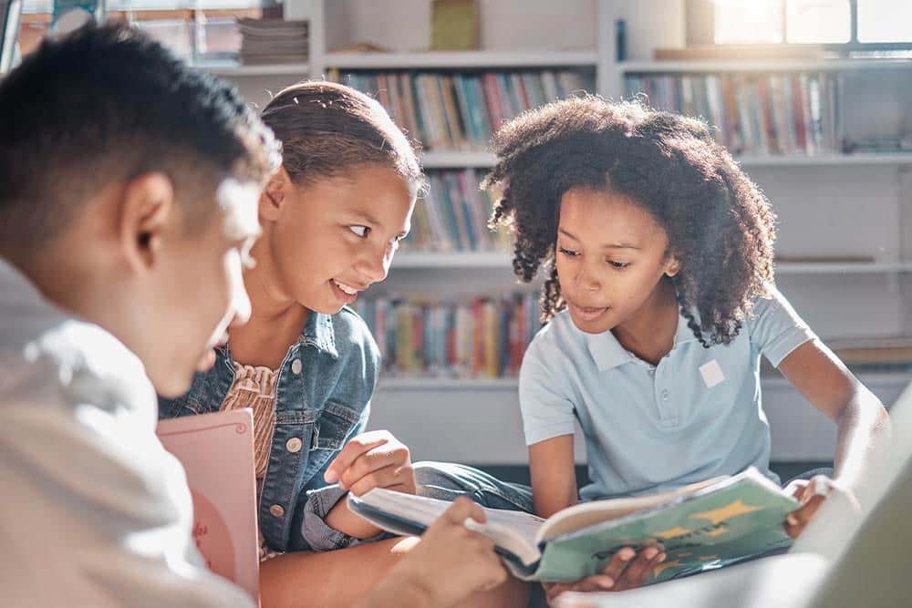 Drie kinderen bladeren samen door kinderboeken van De Kleurrijke Kinderboekenlijst