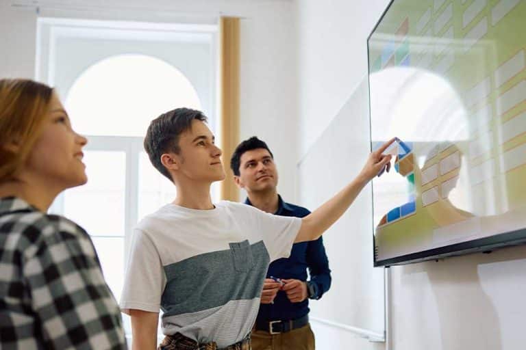 Twee leerlingen en een leerkracht werken met het digibord in de klas