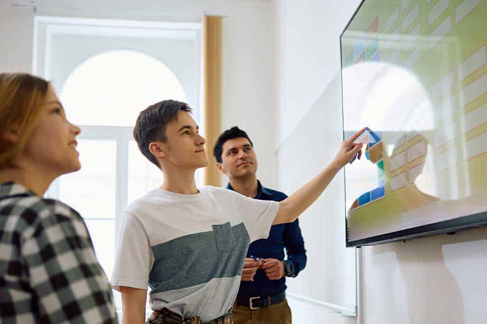 Twee leerlingen en een leerkracht werken met het digibord in de klas