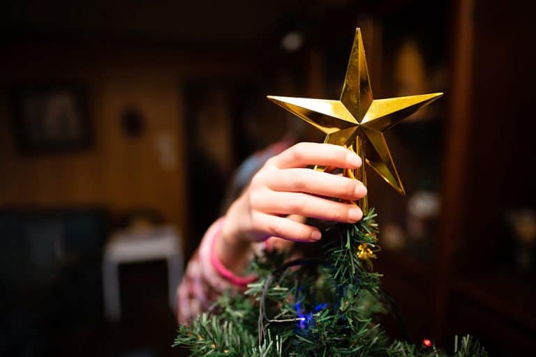 Een kind zet de piek op een kerstboom tijdens het kerstfeest op school