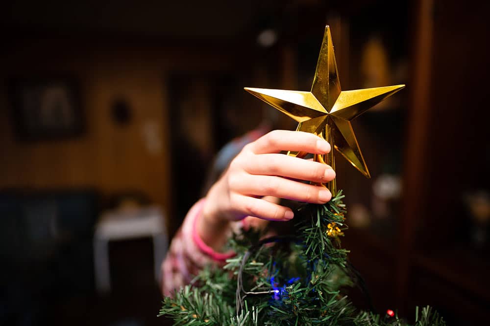 Een kind zet de piek op een kerstboom tijdens het kerstfeest op school