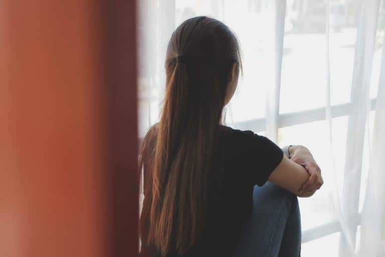Een meisje kijk verdrietig uit het raam met haar armen over elkaar
