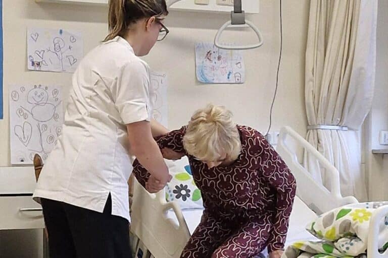 Een student helpt een client uit bed tijdens Skills Heroes