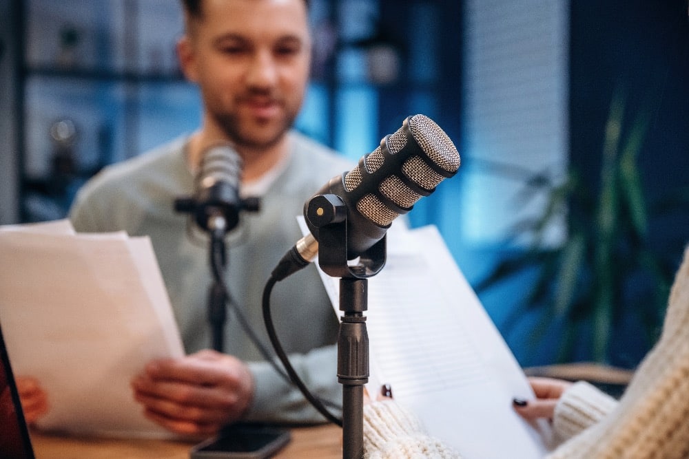 Twee docenten nemen achter een microfoon een podcast op