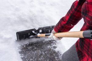 Een leerling maakt het schoolplein schoon met een sneeuwschep