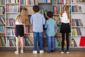 Vier kinderen staan voor een boekenkast in de schoolbibliotheek