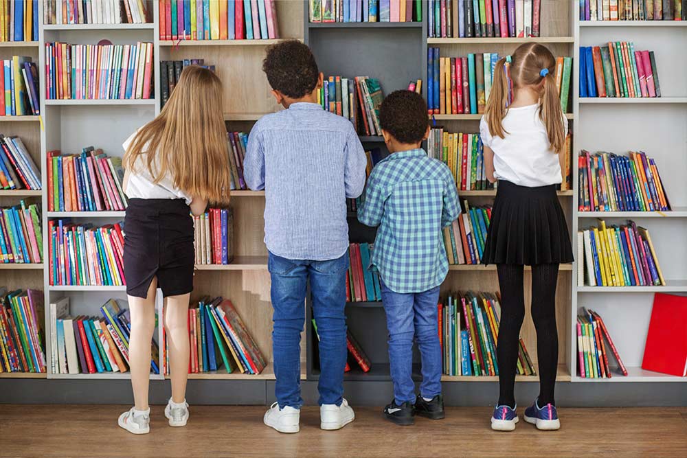 Vier kinderen staan voor een boekenkast in de schoolbibliotheek