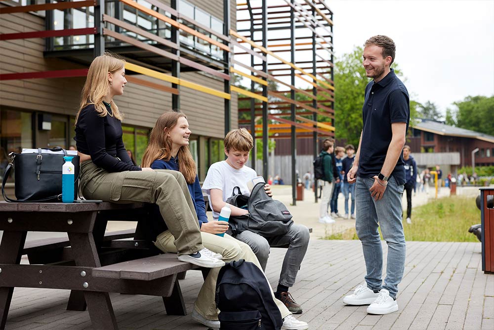 Een docent praat met een groepje leerlingen op het schoolplein