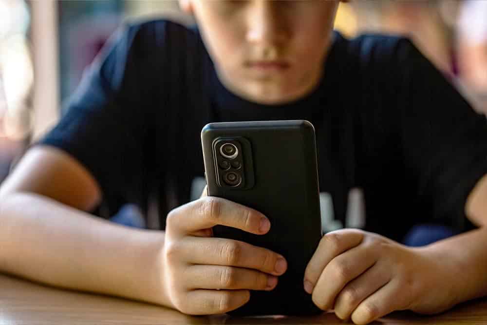 Een kind kijkt met een smartphone in zijn handen op het meldpunt discriminatie voor kinderen