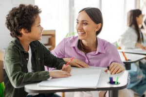 Een leerkracht luistert aandachtig naar een kind in de klas