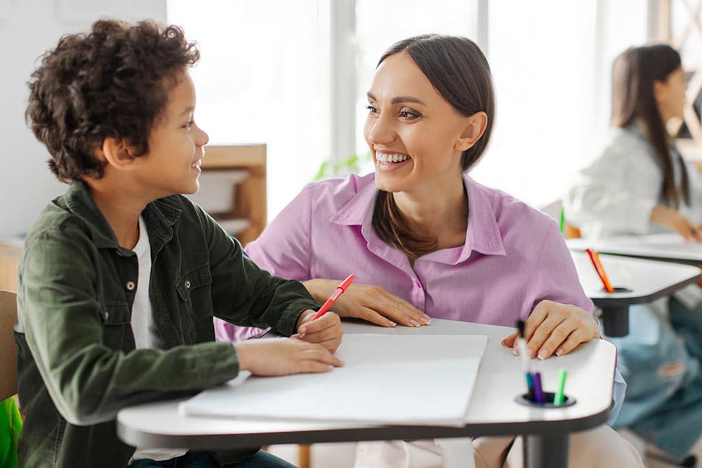 Een leerkracht luistert aandachtig naar een kind in de klas