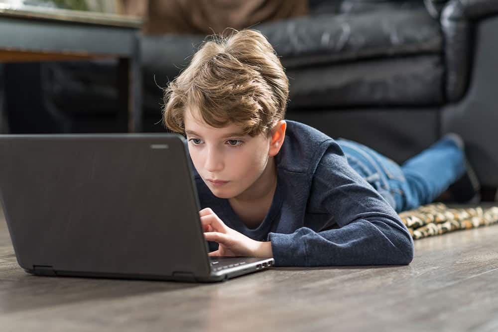 Een kind ligt op zijn buik en kijkt gefocust naar een laptop